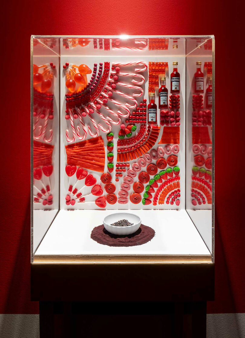 glass display case with red colored candy attached to back wall with white bowl filled with brown dust
