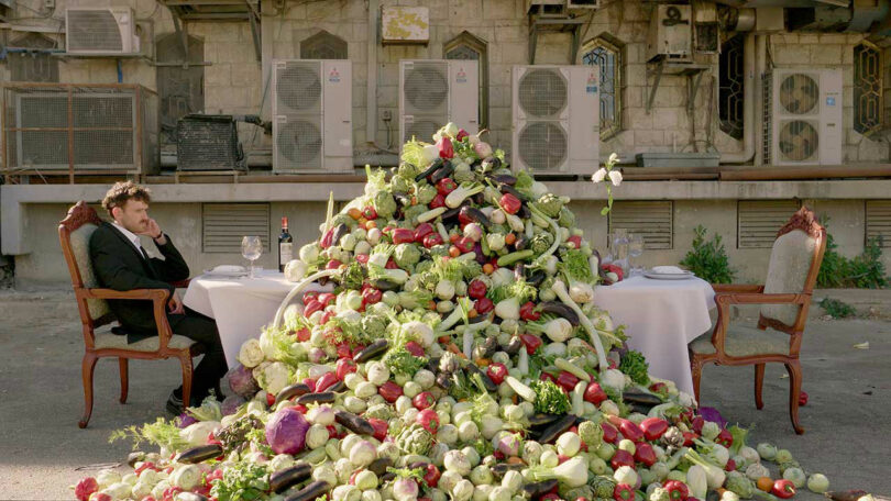 enormous pile of salad like food in front of outdoor dining table with one man sitting in chair