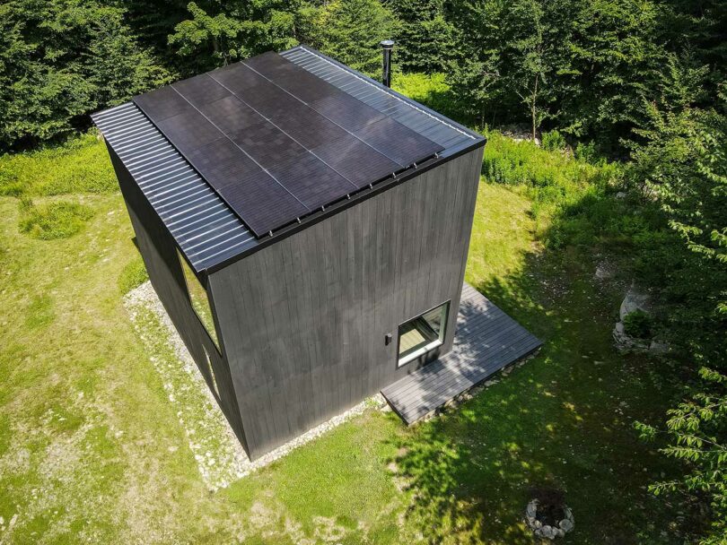 sky view looking down at exterior and roof of black box house surrounded by trees.