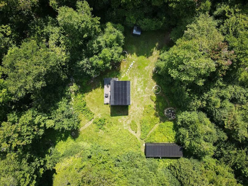 sky view looking down at exterior and roof of black box house surrounded by trees.