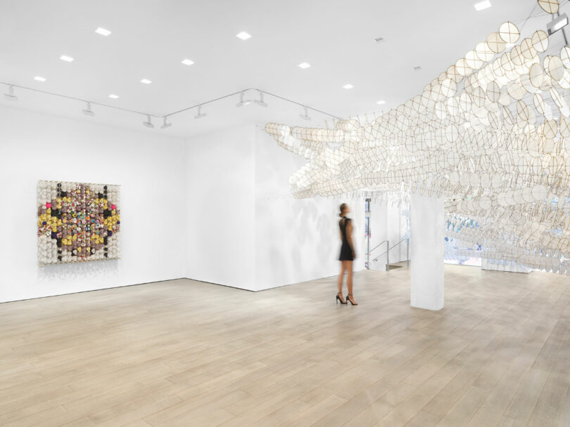 Woman stands under hundreds of white paper kites at gallery entrance