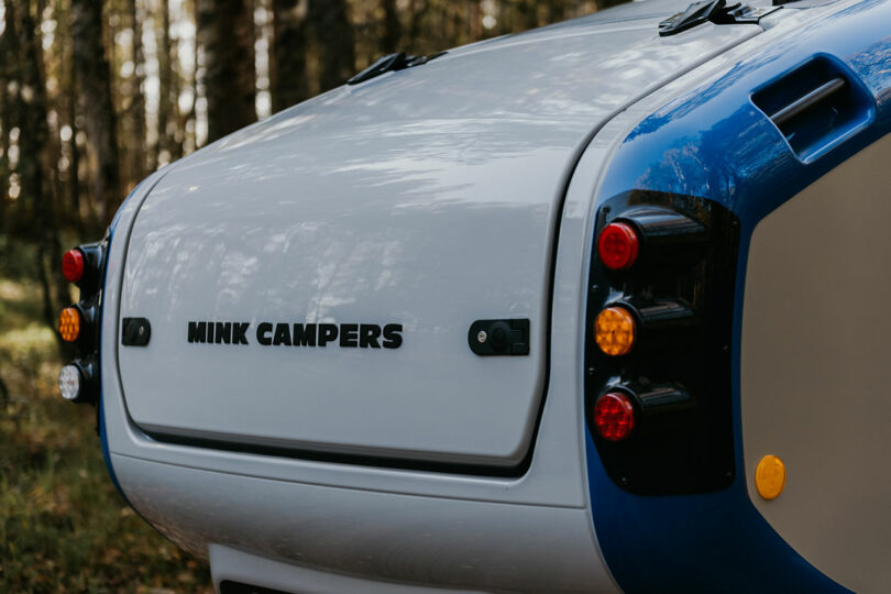 closeup angled side view of gray and blue teardrop camper in woods