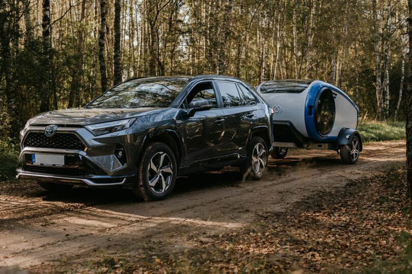 newer dark SUV on forest road pulling gray and blue teardrop camper