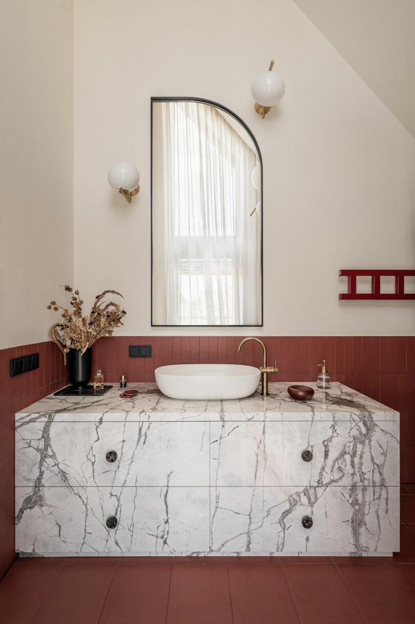 modern bathroom with floating marble vanity and mauvy red tile surround.
