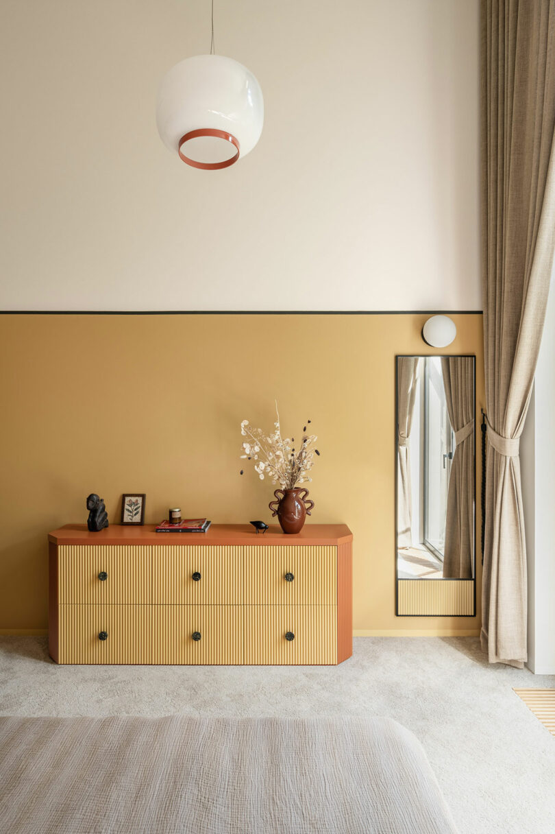 partial view in modern bedroom with half gold painted wall and wood and pink dresser in front