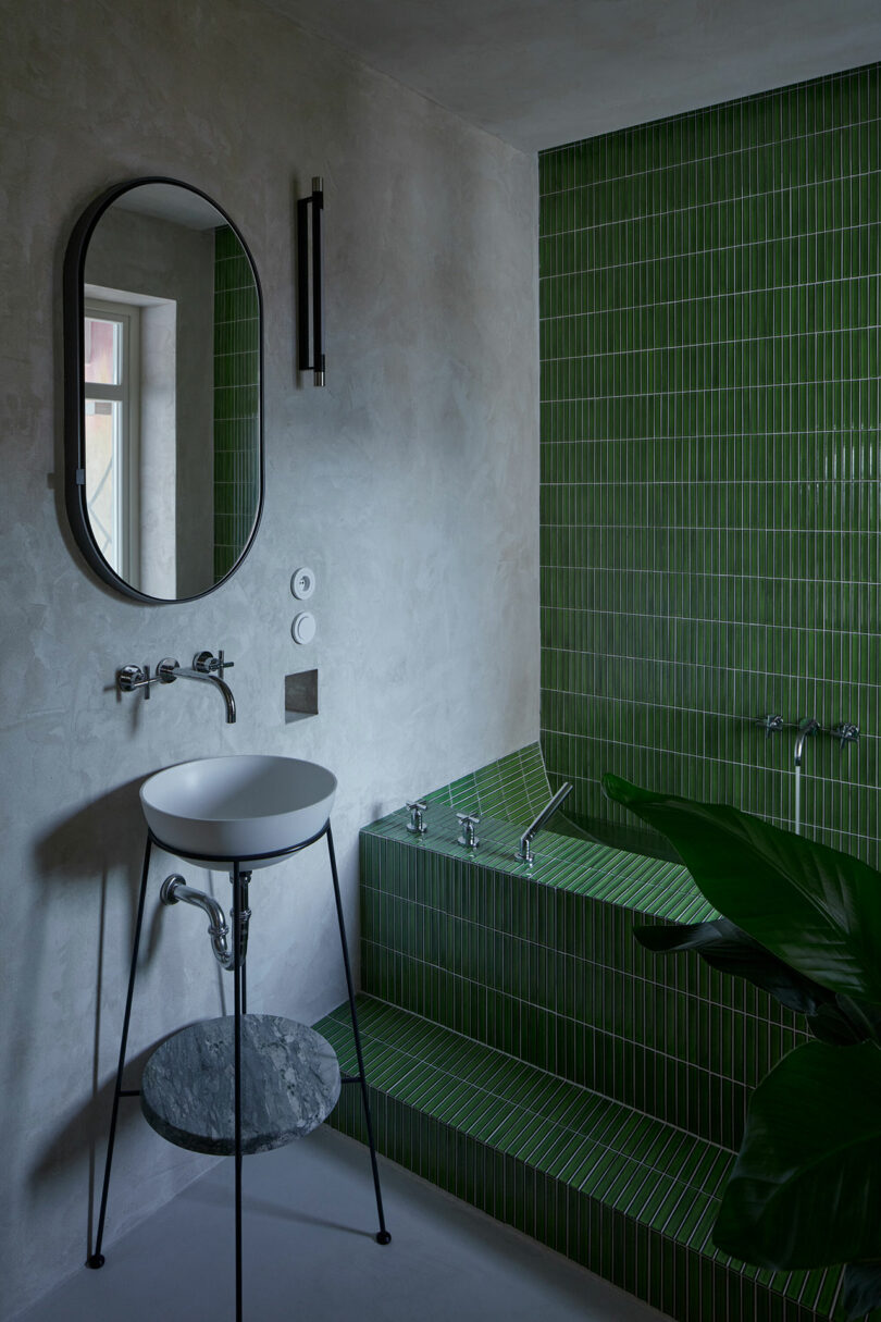 angled view of modern bathroom with green tiled tube and small sink