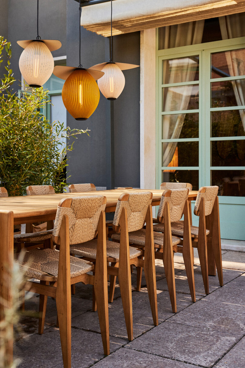 neutral toned outdoor dining space with dining table and ten chairs and three hanging light fixtures