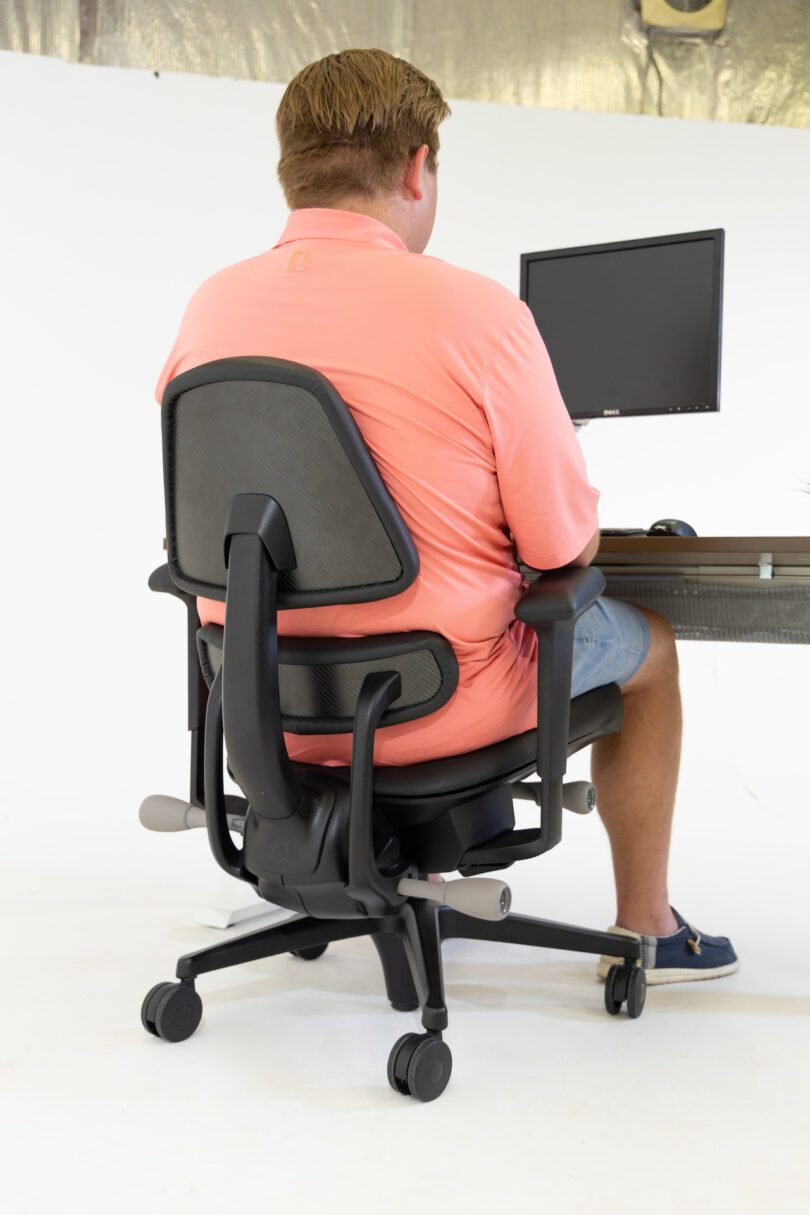 back view of man sitting on black task chair at desk with computer