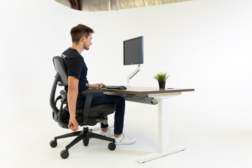 man adjusting task chair at desk with computer
