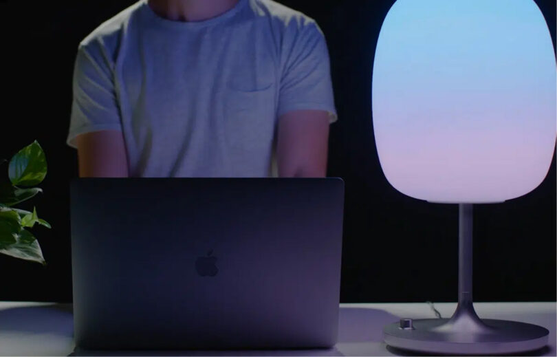 Young man in soft gray pocket t-shirt at his MacBook Pro with SKYVIEW 2 Pro lamp to his left.