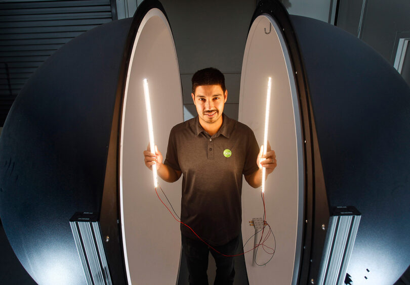 BIOS and SKYLIGHT co-founder, Robert Soler, standing between two large halves of a sphere with white interior holding LED wands of light, illuminating his face in a warm glow.