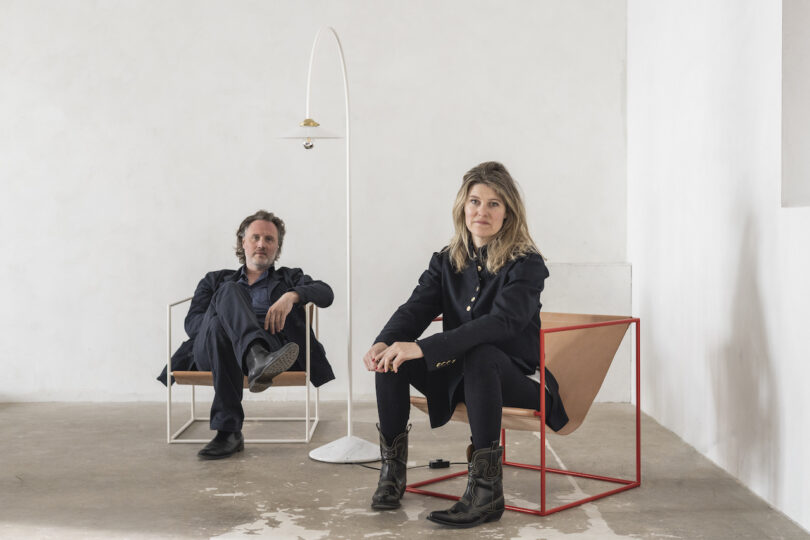 man and woman sitting on minimalist chairs next to white floor lamp