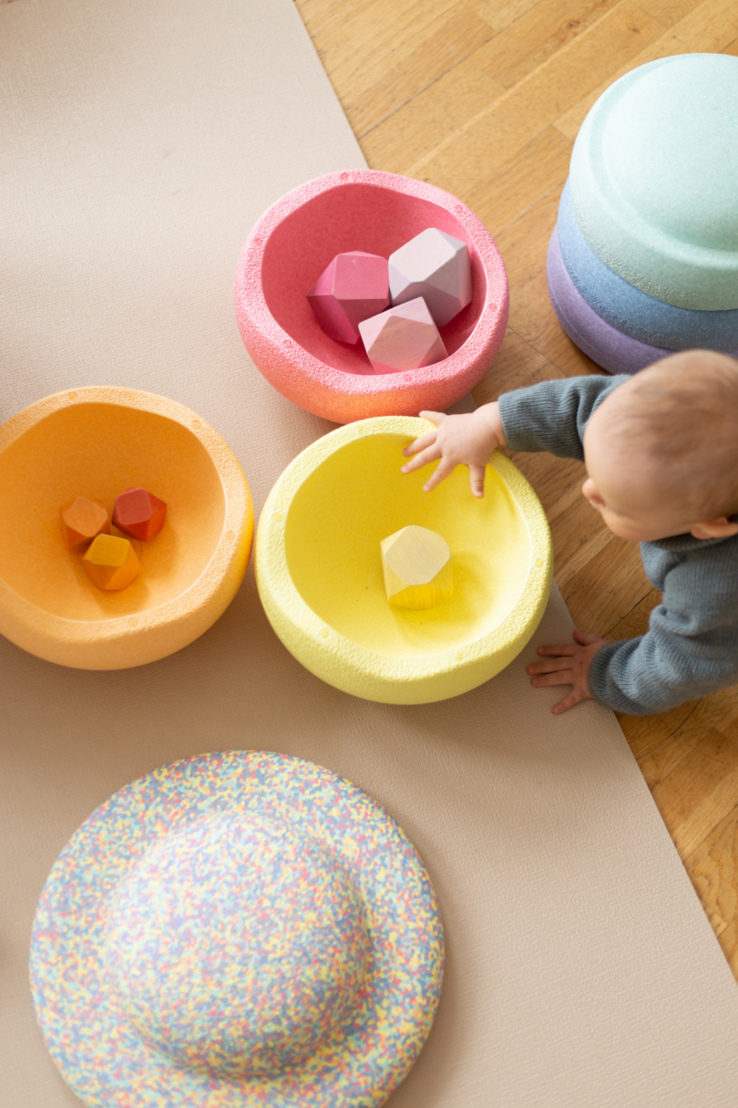 baby reaching for toy inside yellow toy bowl 