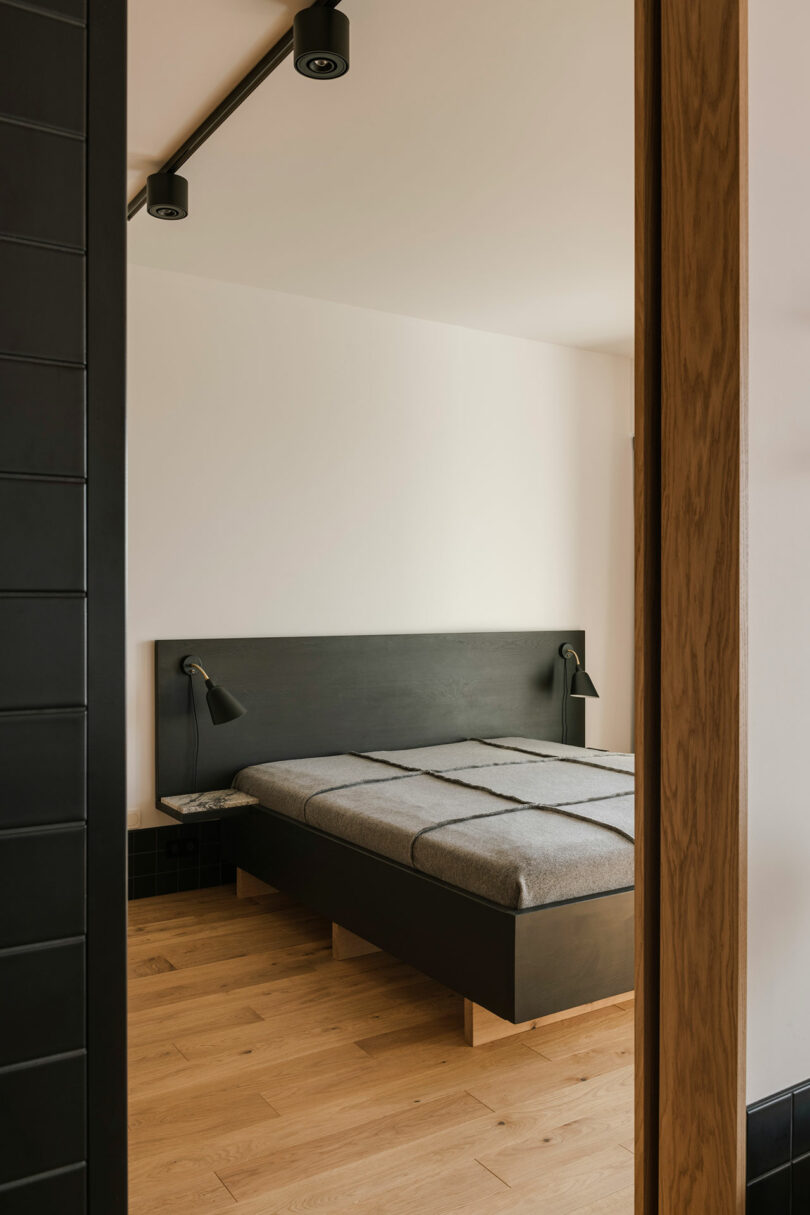angled view looking through doorway into minimalist modern bedroom with black headboard and simple bedding
