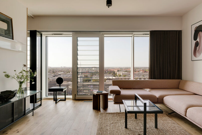 interior shot of modern living room in an apartment with sectional sofa and wall of windows overlooking city