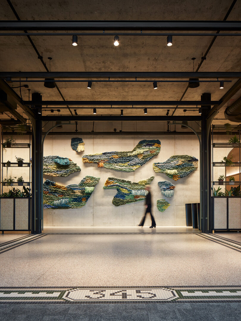 a person walking in front of a large textile wall art installation in earthy hues