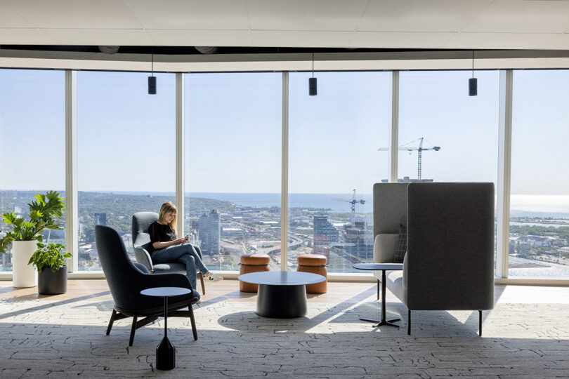 a person sits in a chair in front of a wall of floor to ceiling windows in an office