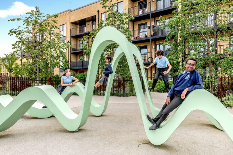 large seafoam green abstract undulating outdoor interactive art installation with children playing on it