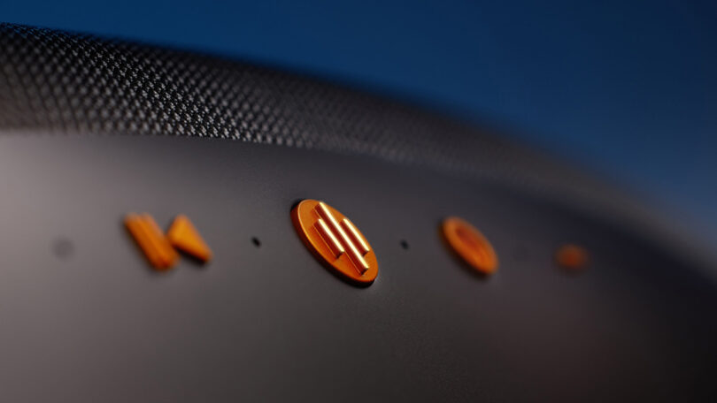 Detail of Papaya Orange colored buttons set against Galvanic Grey body of the Bowers & Wilkins Zeppelin McLaren Edition wireless speaker.