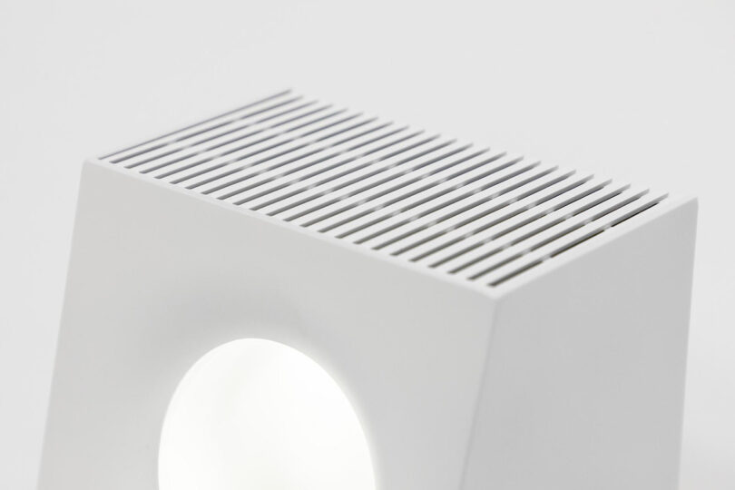 Top detail of the speaker grill of the square-shaped white audio device with small circular window containing a globule of nanoscale ferromagnetic particles designed to move in relation to music.
