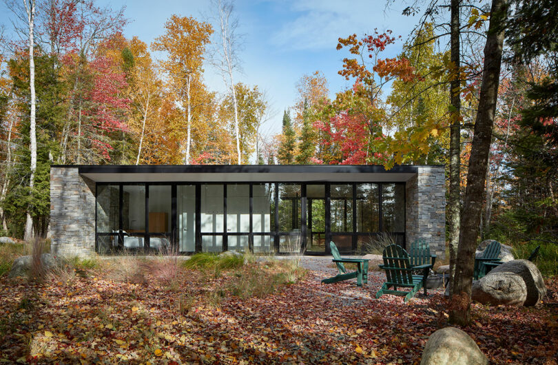 exterior shot of a one-story rectangular stone house surrounded by forest