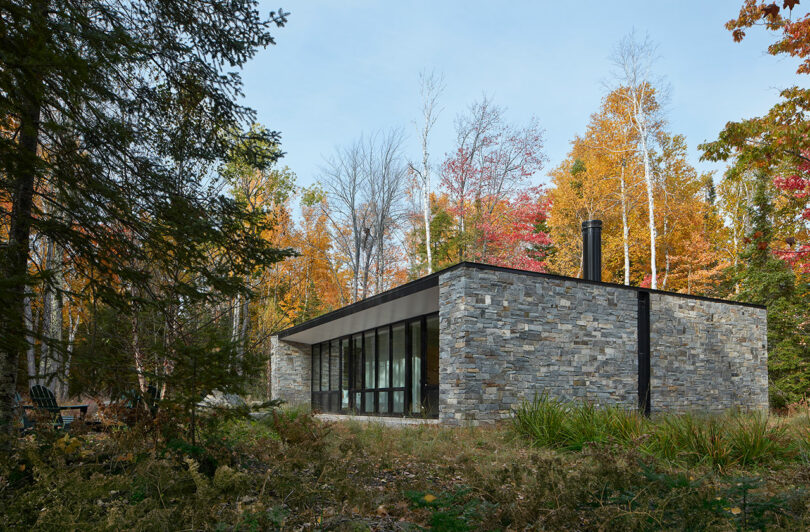 angled exterior shot of a one-story rectangular stone house surrounded by forest