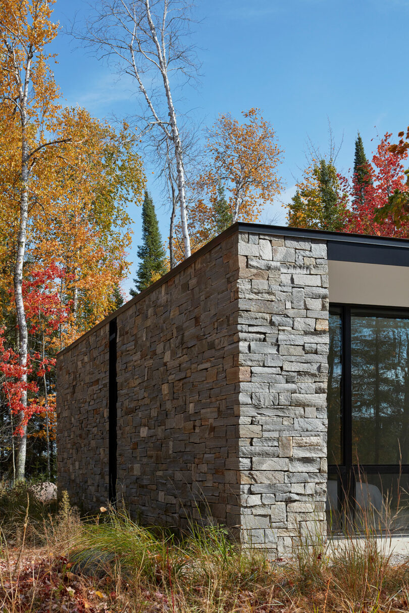 closeup end exterior shot of a one-story rectangular stone house surrounded by forest