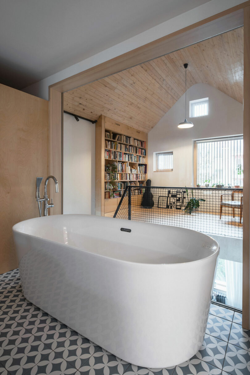 angled shot of modern bathroom with white bathtub in front of large window overlooking living room below