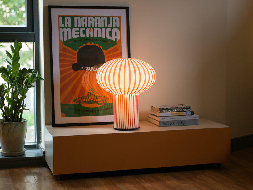 mushroom-shaped orange and white striped table lamp illuminated on a styled console