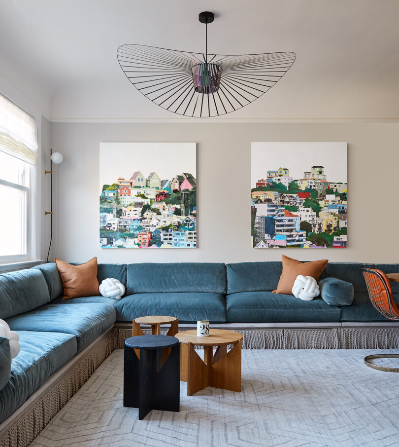 large styled living space with a built-in L-shaped turquoise sofa, three small tables, two large pieces of art, and a statement making light fixture