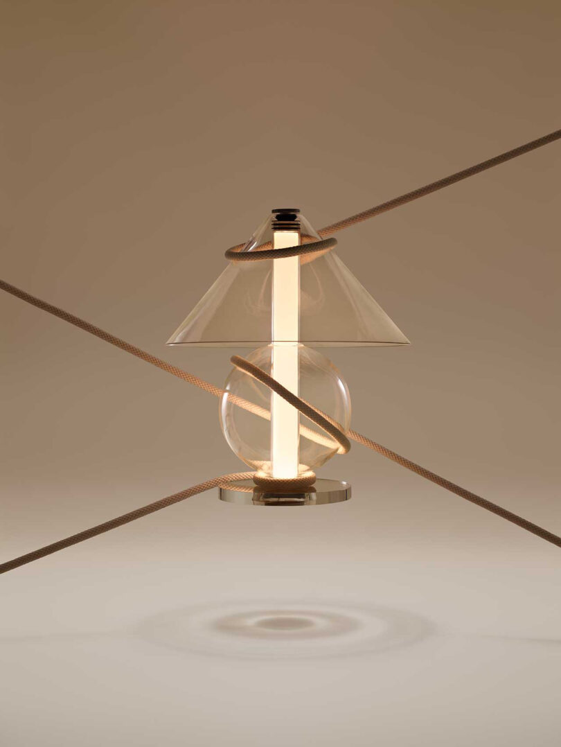 all glass lamp with round base and cone-shaped shade illuminated held up by ropes