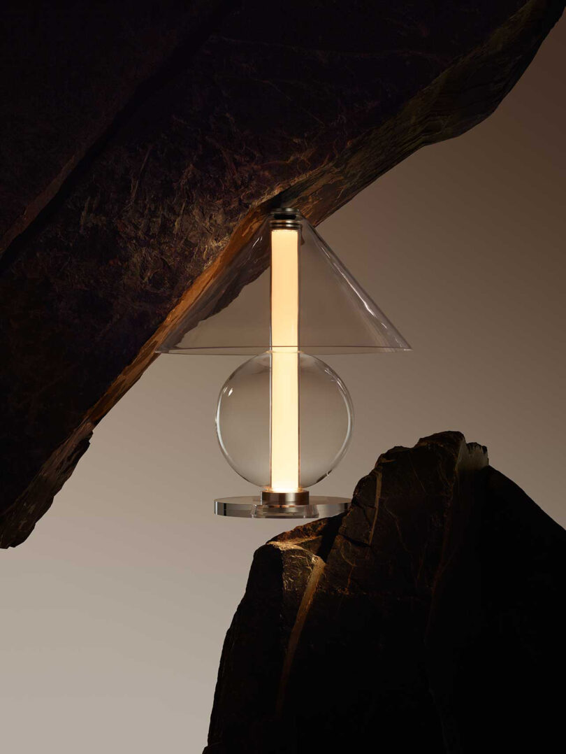all glass lamp with round base and cone-shaped shade illuminated balanced between two rocks