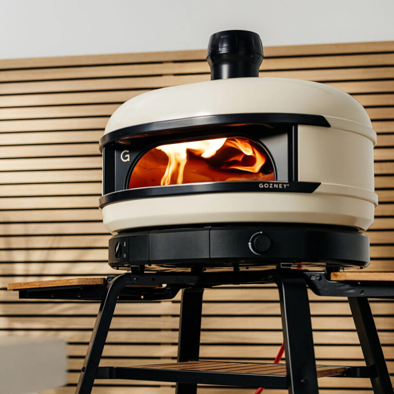 Light tan dome shaped pizza oven with visible fire flame inside