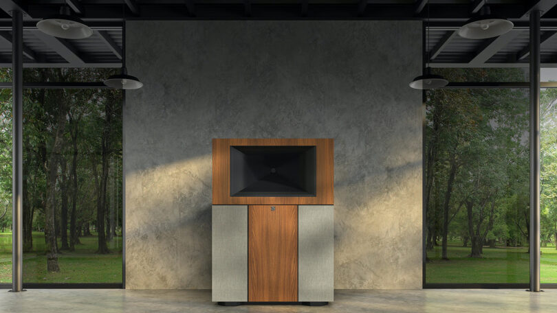 large wood horn based floor standing audio speaker set in modernist room with forest exterior viewable from surrounding windows.