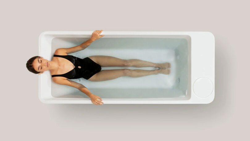 woman in black one-piece bathing suit laying in a white cold plunge pool as seen from overhead