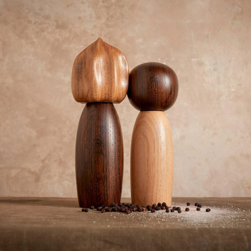 abstract figurine shaped wooden salt and pepper mill grinders with pieces of peppercorns and salt spilled at their base