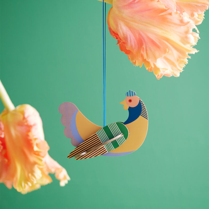 multicolor flat-pack chicken ornament hanging against a mint green background