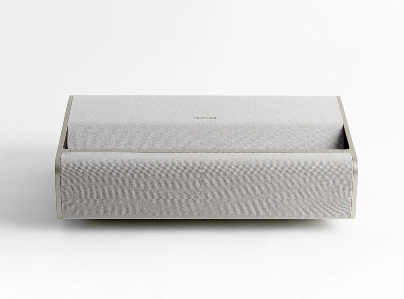 Front view of the soft earth tone fabric covered XGIMI Mira ultra short throw projector. Unit has soft curves and brushed metal edge detailing.