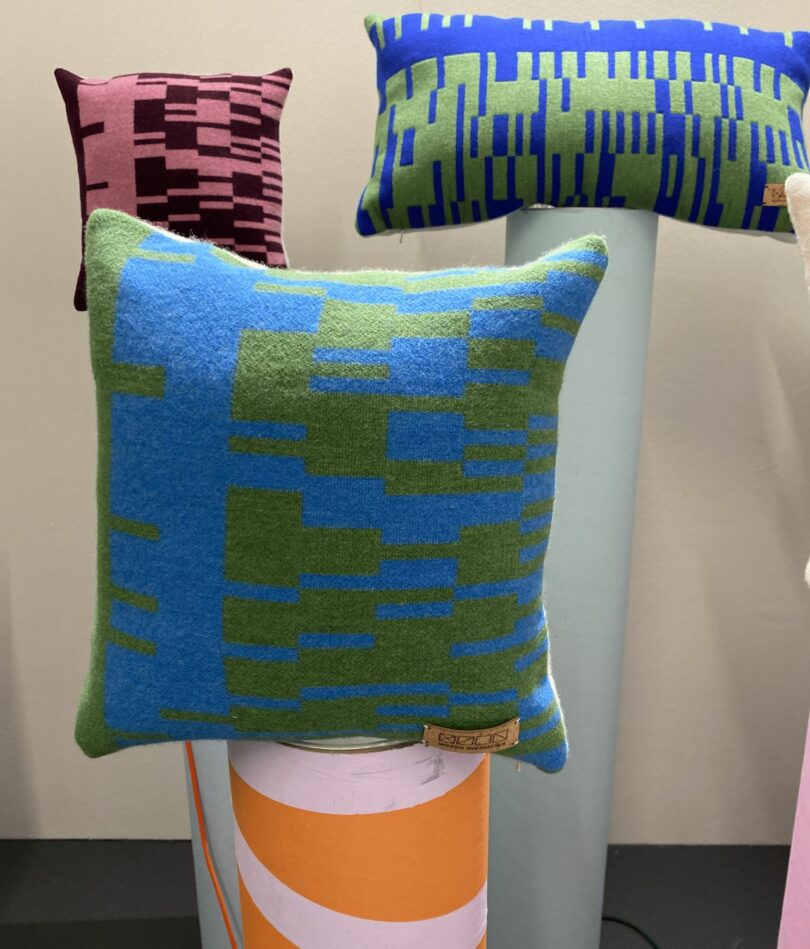 Three brightly colored geometric cushions sit on top of cardboard tubes.