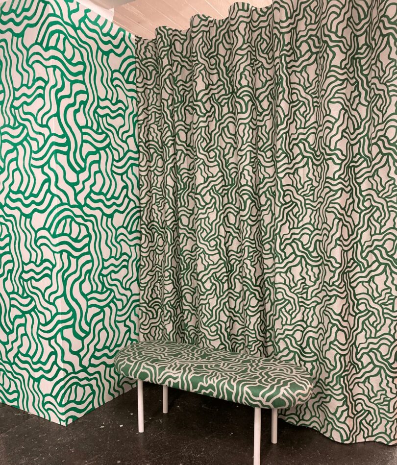 A wall, a curtain and a bench all feature a white background and green squiggly pattern.