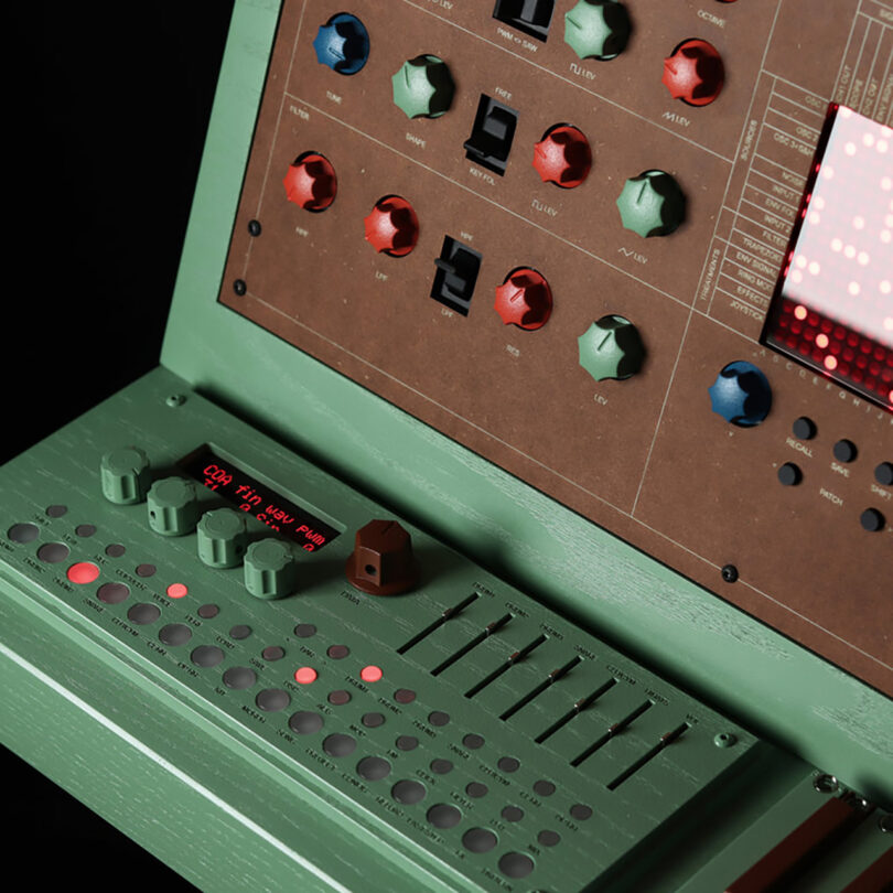 Detail of left hand corner of the ATOM-IC green and brown wood cabinet synthesizer with small keyboard and layout of numerous colorful dials, switches, sliders and buttons controls.