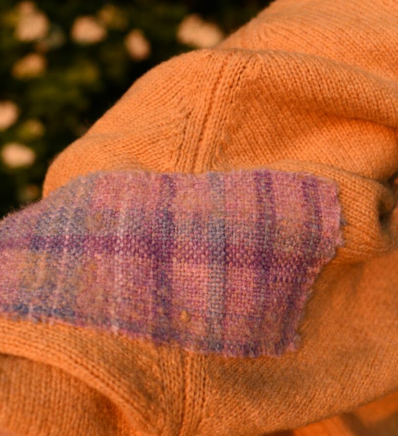 A section of orange jumper with a pink and purple woven patch