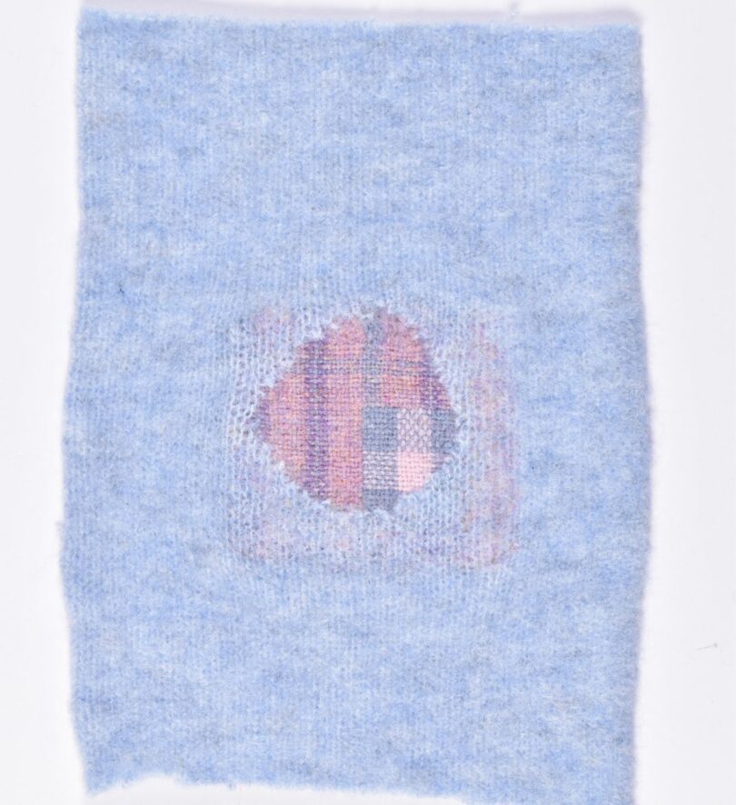 A pale blue sleeve has been patched with a pink and purple woven and felted patch