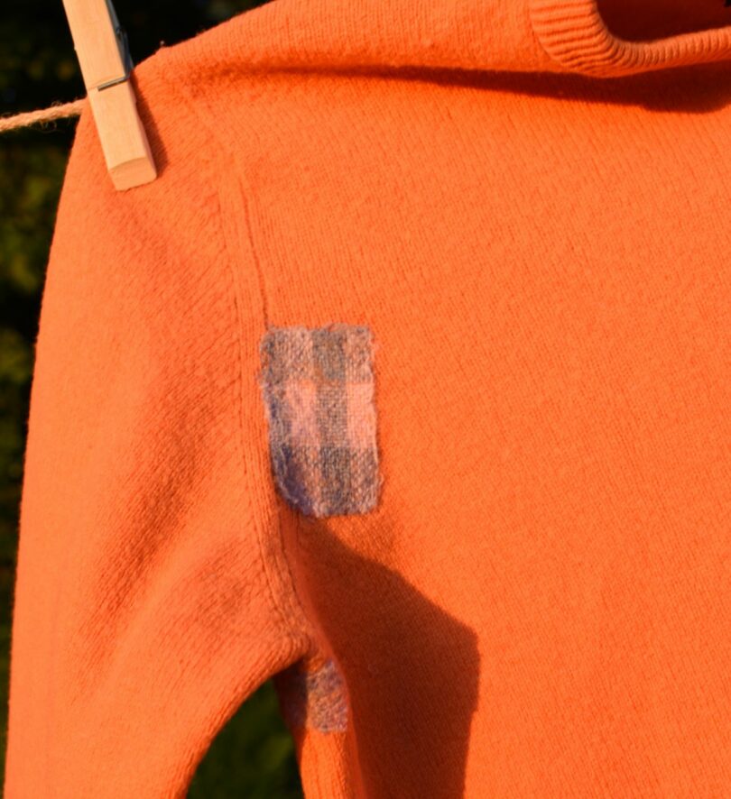 An orange woollen sweater with patches hangs on a line