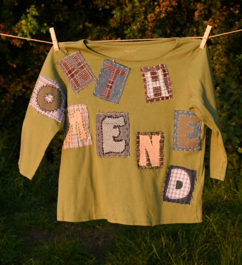 The words "one the mend" are spelled out with patches – each of which has one letter – on a green long-sleeved top hanging on a washing line