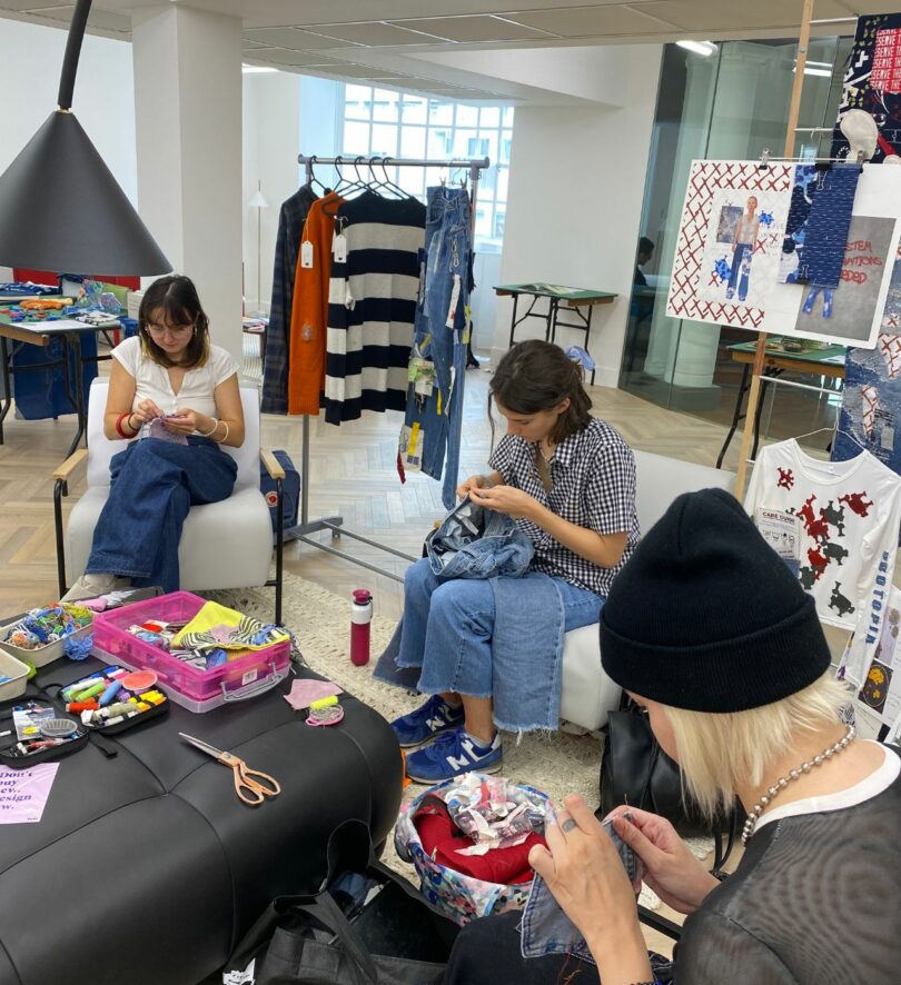 Three white women in their 20s sit in a group mending