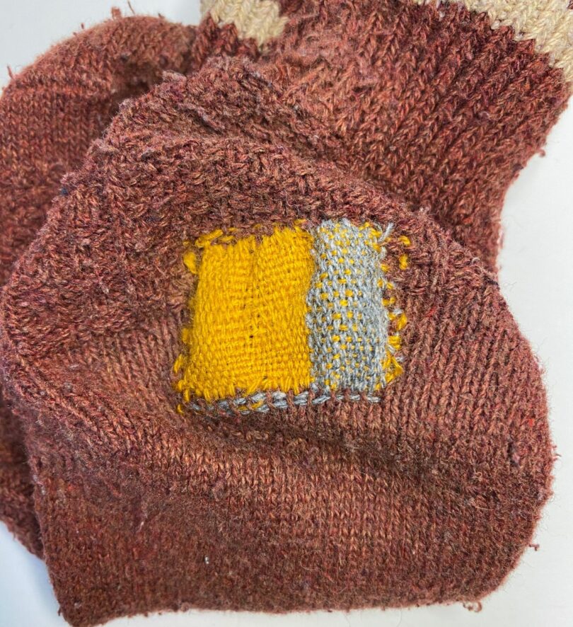 A rusty-colored sock darned in yellow and gray.