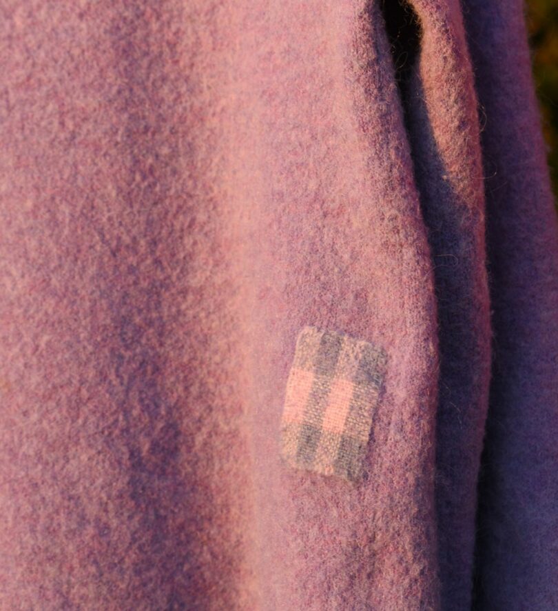 A pink woollen sweater mended with a woven pink and purple patch.