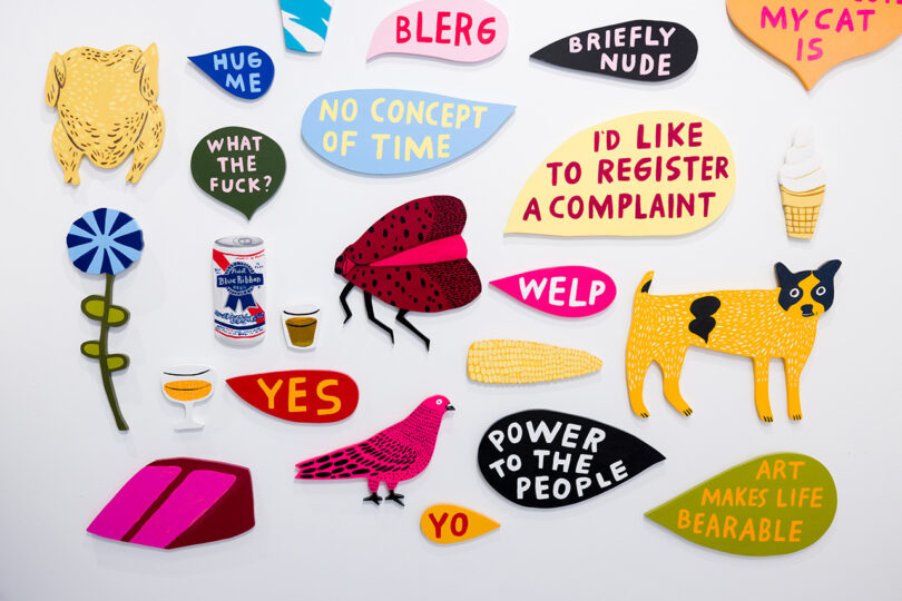 gallery wall filled with small, colorful pieces of painted wood objects and speech balloons