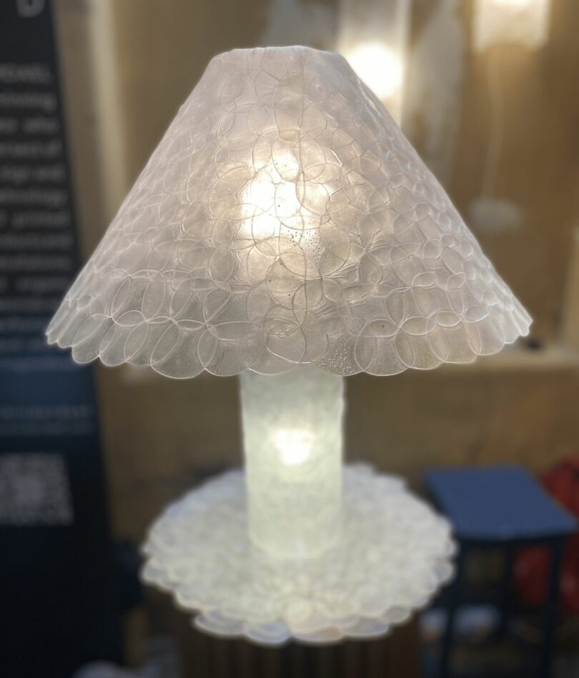 A traditional table lamp form with a tubular stand and conical shade appears to be made from opaque white overlapping circular forms
